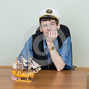 Man in a uniform cap at table with ship