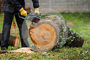 A man in uniform cuts an old tree in the yard with an electric saw