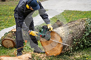 A man in uniform cuts an old tree in the yard with an electric saw