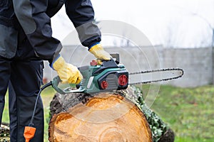 A man in uniform cuts an old tree in the yard with an electric saw