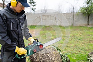 A man in uniform cuts an old tree in the yard with an electric saw