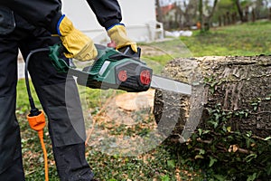 A man in uniform cuts an old tree in the yard with an electric saw