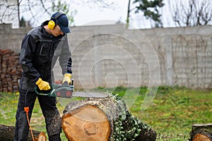 A man in uniform cuts an old tree in the yard with an electric saw