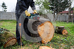 A man in uniform cuts an old tree in the yard with an electric saw