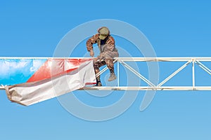 a man in uniform dismantles a sign on a background of blue sky