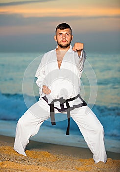 Man in uniform doing taekwondo exercises at sunset sea shore