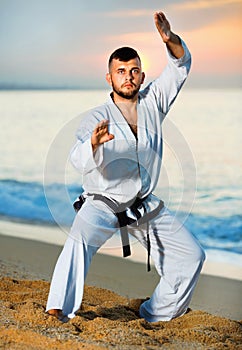 Man in uniform doing taekwondo exercises at sunset sea shore