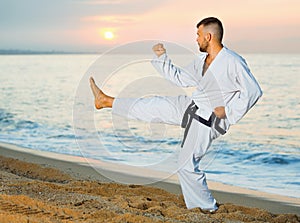 Man in uniform doing taekwondo exercises at sunset sea shore