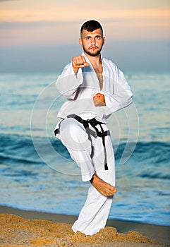 Man in uniform doing taekwondo exercises at sunset sea shore