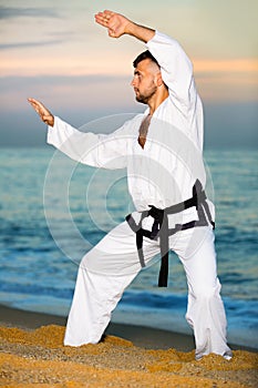 Man in uniform doing taekwondo exercises at sunset sea shore