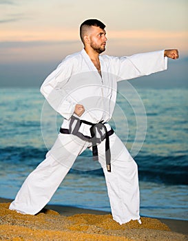 Man in uniform doing taekwondo exercises at sunset sea shore