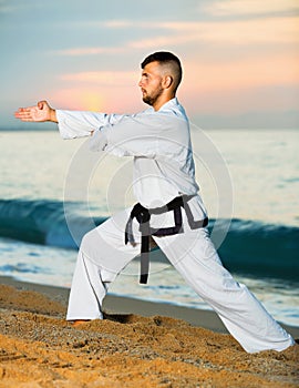 Man in uniform doing taekwondo exercises at sunset sea shore