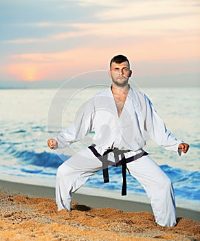 Man in uniform doing taekwondo exercises at sunset sea shore