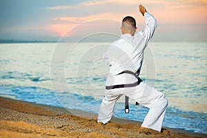 Man in uniform doing taekwondo exercises at sunset sea shore