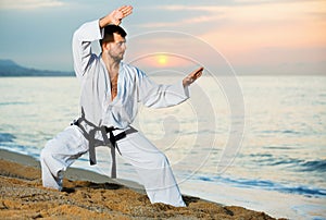 Man in uniform doing taekwondo exercises at sunset sea shore