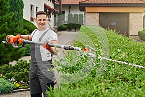 Man in uniform shaping bushes with electric trimmer