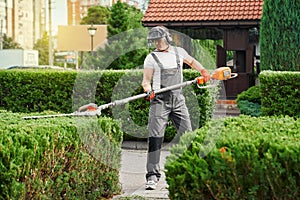 Man in uniform trimming bushes during warm sunny day