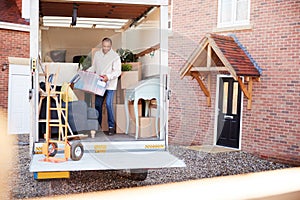 Man Unloading Furniture From Removal Truck Outside New Home On Moving Day