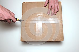Man unpacking box with cutter. View from above. The concept of delivery and verification of online purchases or opening a gift