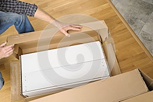 A man is unpacking a cardboard box with furniture