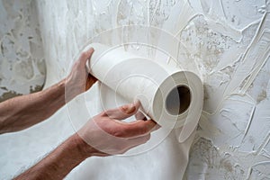 Man unraveling a rolled white wallpaper, illustrating home renovation and interior design in process