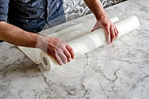 Man unraveling a rolled white wallpaper, illustrating home renovation and interior design in process