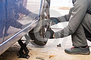 A man unscrews a car wheel in a garage. Replacing car wheels