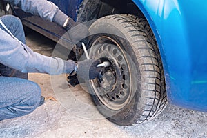 A man unscrews a car wheel in a garage. Replacing car wheels