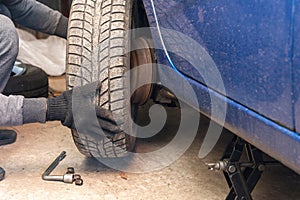 A man unscrews a car wheel in a garage. Replacing car wheels