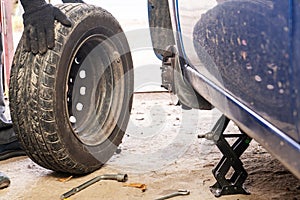 A man unscrews a car wheel in a garage. Replacing car wheels