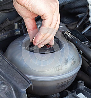 A man unscrews the expansion tank cap of a car with coolant, close-up. Engine overheating problem, airlock