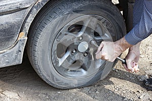 A man unscrews a flat car tire outdoors. Wheel replacement