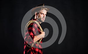 Man unshaven cowboy black background. Lasso can be tied or wrapped. Western life. Man wearing hat hold rope. Lasso tool