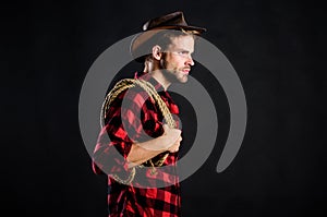 Man unshaven cowboy black background. Man wearing hat hold rope. Lasso tool of American cowboy. Lasso is used in rodeos