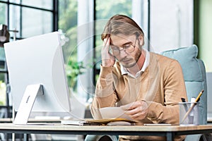 Man upset in office reading message on paper, businessman received mail envelope with notification and bad news, sitting