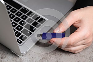 Man with usb flash drive near laptop at grey table, closeup