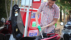 Man use gas pump nozzle filling gasoline fuel to tank of motorcycle in oil station. Thailand. 1920x1080