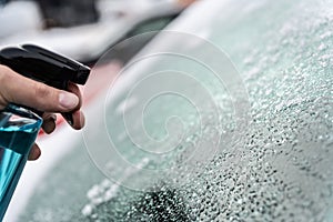 Man uses a bottle of de-icer to defrost the ice-covered windshield