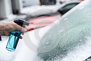 Man uses a bottle of de-icer to defrost the ice-covered windshield