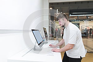 Man uses a computer in a modern electronics store. Buyer selects a monoblock in a light tech store