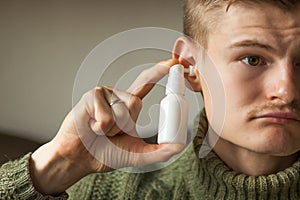 Man uses an ear spray. Man& x27;s hand holds a white ear spray bottle with nozzle installed in the ear hole. Daily