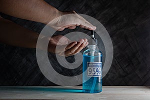 Man uses hand sanitizer blue gel with ingredient ethyl alcohol 95% on wooden table with dark background