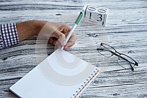 Man uses his left hand to wright in a notebook. Glasess and calendar with 13th of August. Conceptual photo of lefthanded