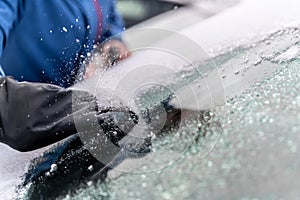 man uses ice scrapers to thaw car windshield