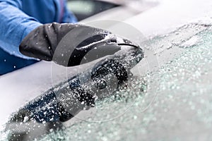 man uses ice scrapers to thaw car windshield