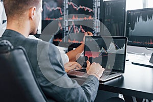 Man uses laptop. Team of stockbrokers works in modern office with many display screens