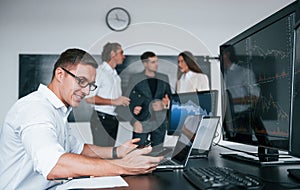 Man uses laptop. Team of stockbrokers works in modern office with many display screens