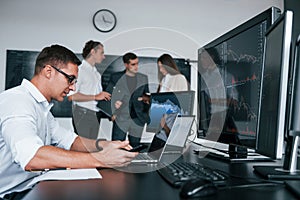 Man uses laptop. Team of stockbrokers works in modern office with many display screens