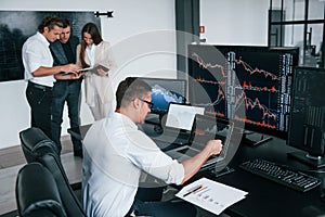 Man uses laptop. Team of stockbrokers works in modern office with many display screens