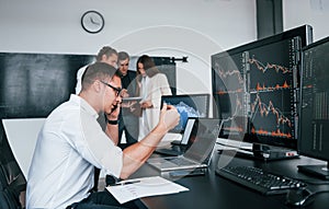 Man uses laptop. Team of stockbrokers works in modern office with many display screens